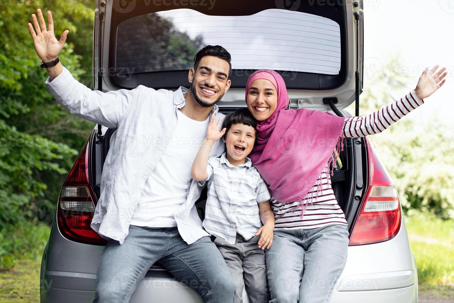 Portrait Of Happy Arab Family With Little Son Sitting In Car Trunk And Smiling At Camera, Excited Muslim Parents And Their Male Child Enjoying Traveling With Automobile Together, Free Space photo