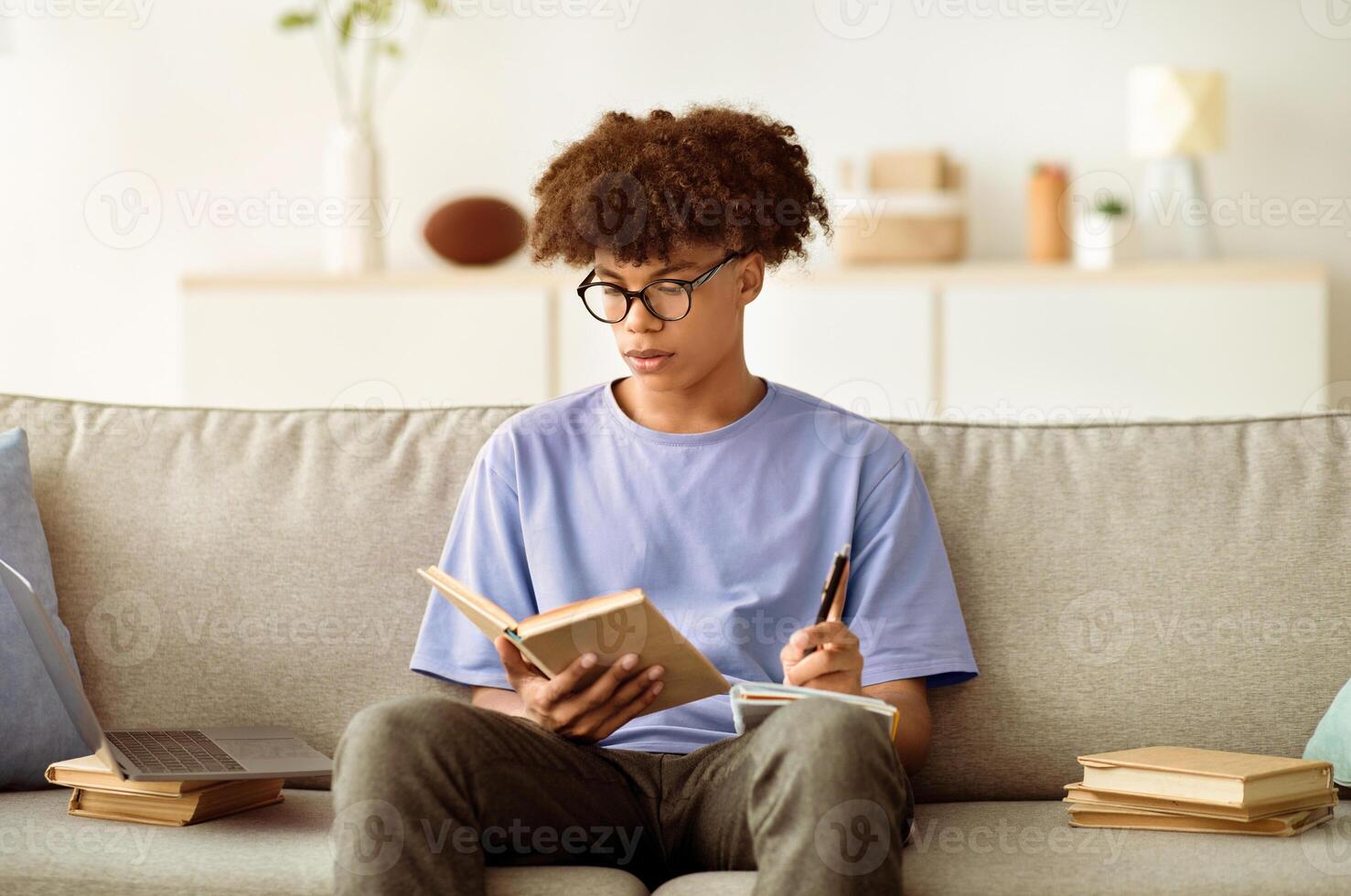 Focused black adolescent with textbook taking notes, studying at home, preparing for important exam. Smart African American teen student learning remotely during coronavirus quarantine photo