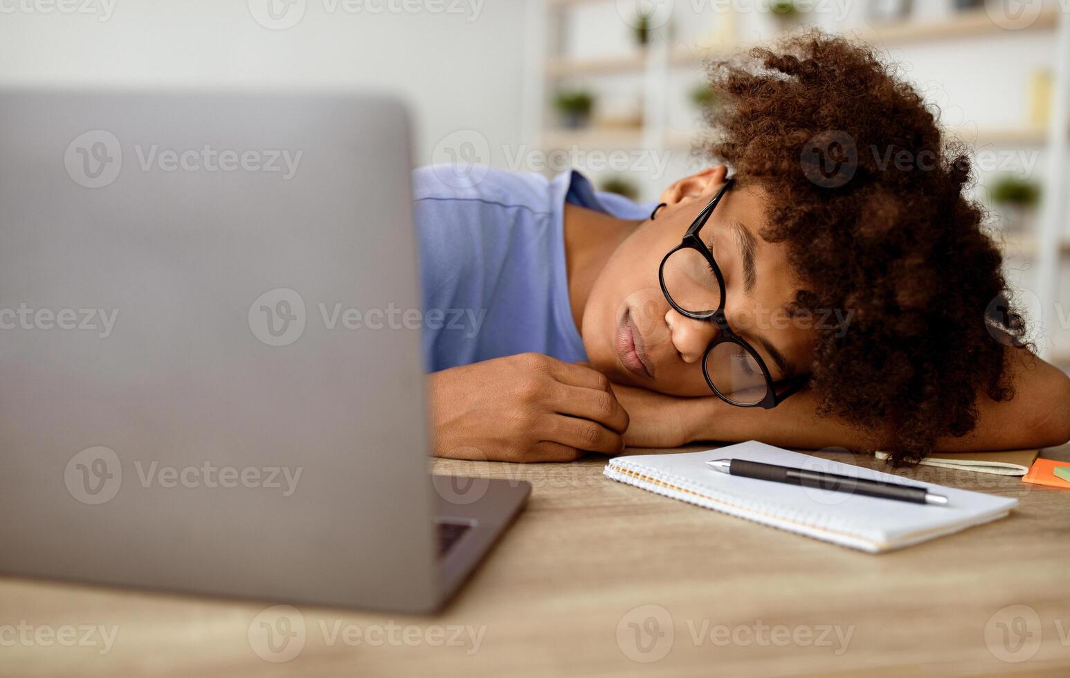 Tired black teenager sleeping on table in front of laptop computer at home, panorama. Exhausted African American teen student overworking during online studies, getting ready for remote exam photo