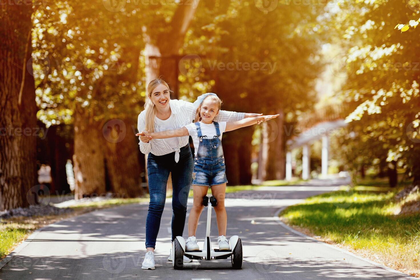 Family Fun. Mother Teaching Daughter To Ride A Segway Spending Weekend In City Park Outside. Copy Space photo