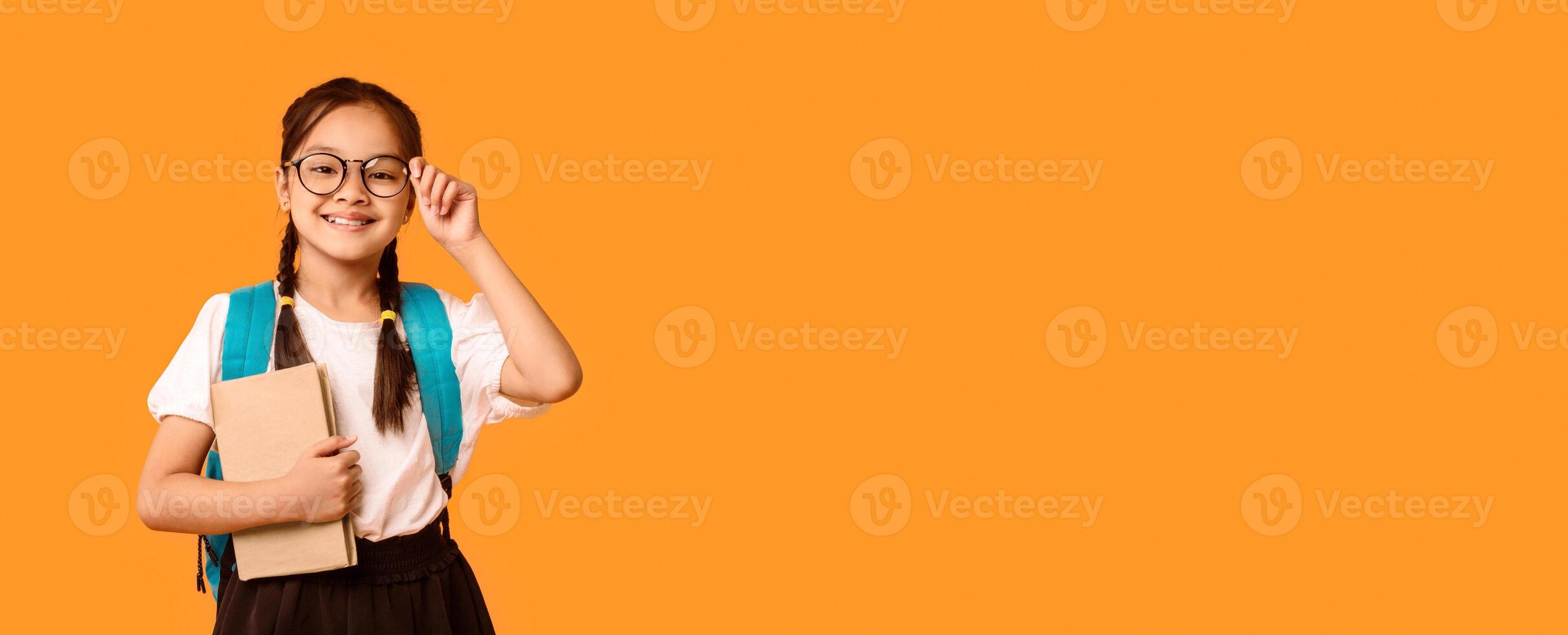 Back To School Concept. Joyful Korean Kid Girl Holding Book Smiling To Camera Posing Over Yellow Studio Background. photo