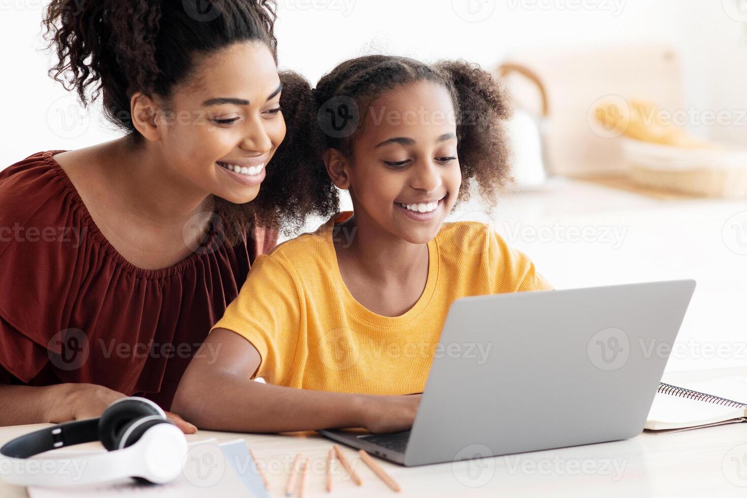Cute black mother and kid using laptop together, sitting at kitchen table, hugging and looking at computer screen, spending time together, watching cartoon, copy space, closeup photo