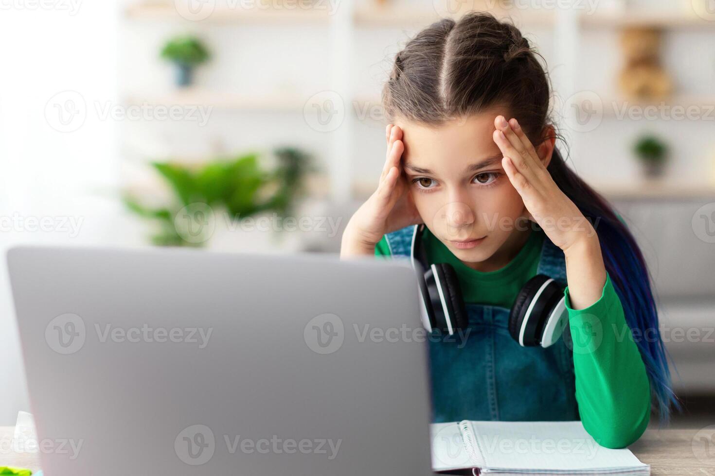 Bored Young Female Pupil Sitting At Desk With Laptop Computer At Home, Tired Upset Adolescent Having Problems With Online Education, Suffering Difficulties With Distance Learning photo