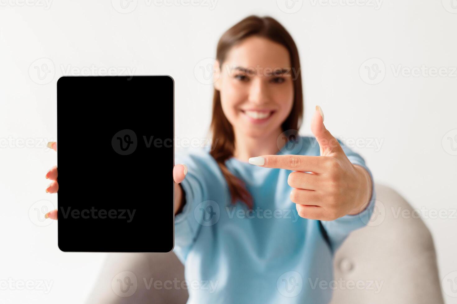 Joyful millennial woman pointing at tablet with blank screen for mockup, promoting new app, offering space for website or advertisement, selective focus. Touch pad display template photo
