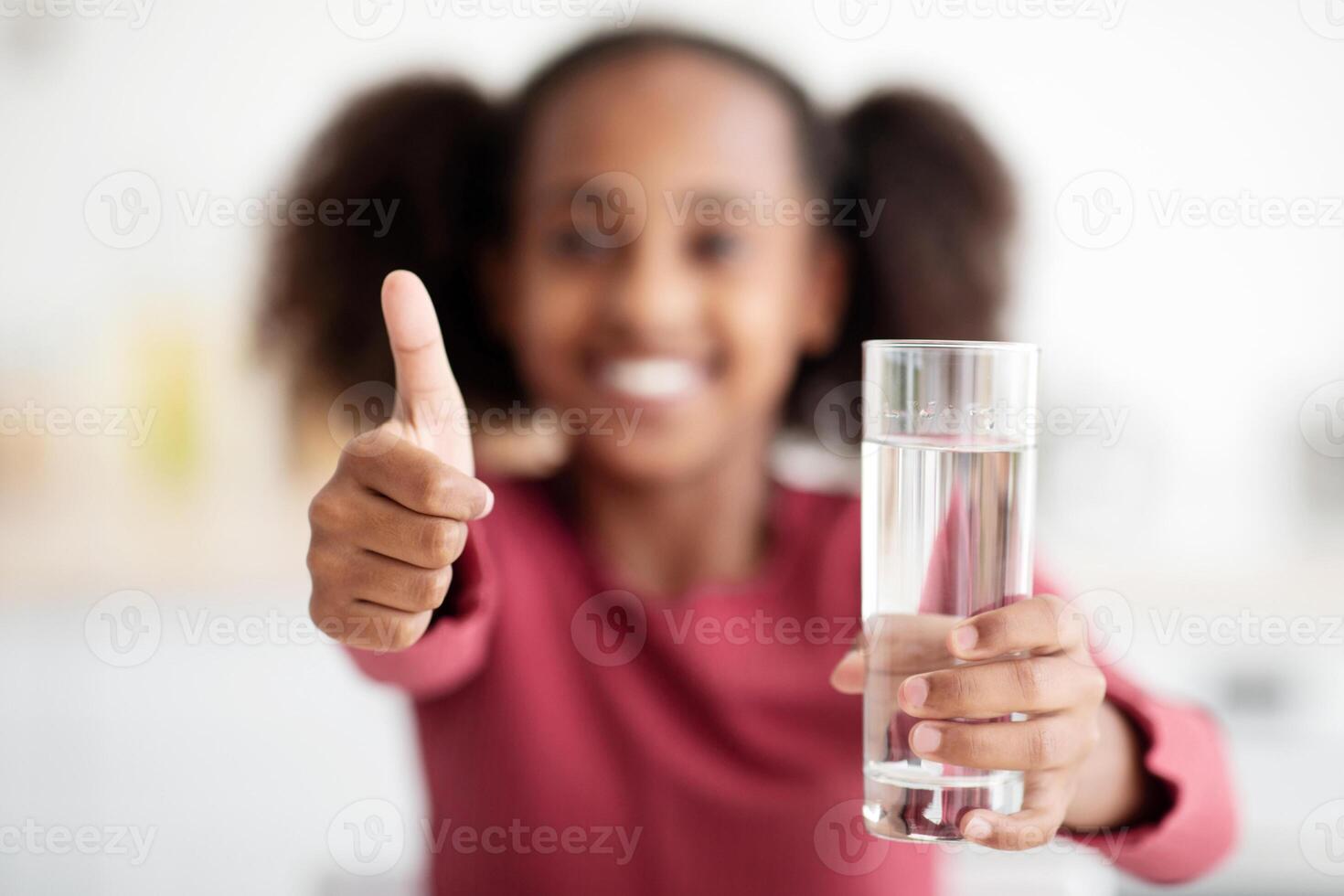 Selective focus on glass of water and thumb up, unrecognizable black girl drinking water, african american teen kid recommending fresh spring water, closeup. Kids hydration cocnept photo