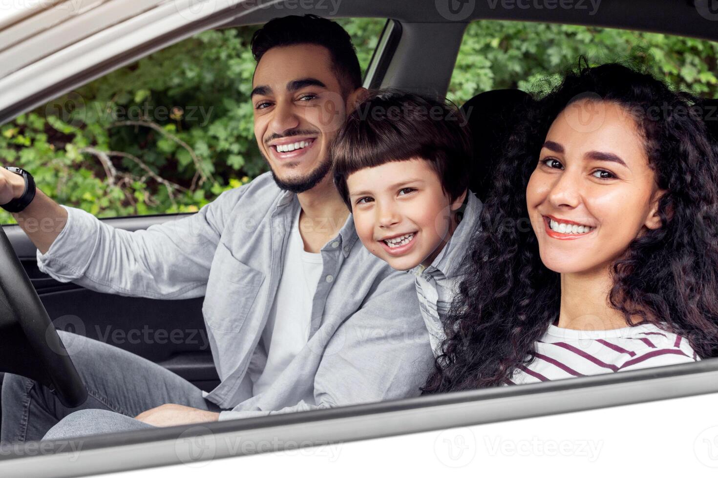 Smiling young arab man and woman with child are driving in car and looking at camera from open window, outdoor, panorama. Travel with family in summer, road and vacation together travel by automobile photo