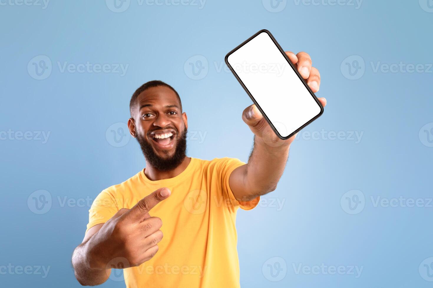 New awesome mobile app. Overjoyed African American guy pointing at smartphone with blank white screen on blue background, mockup. Cellphone display template, space for advertisement or website photo