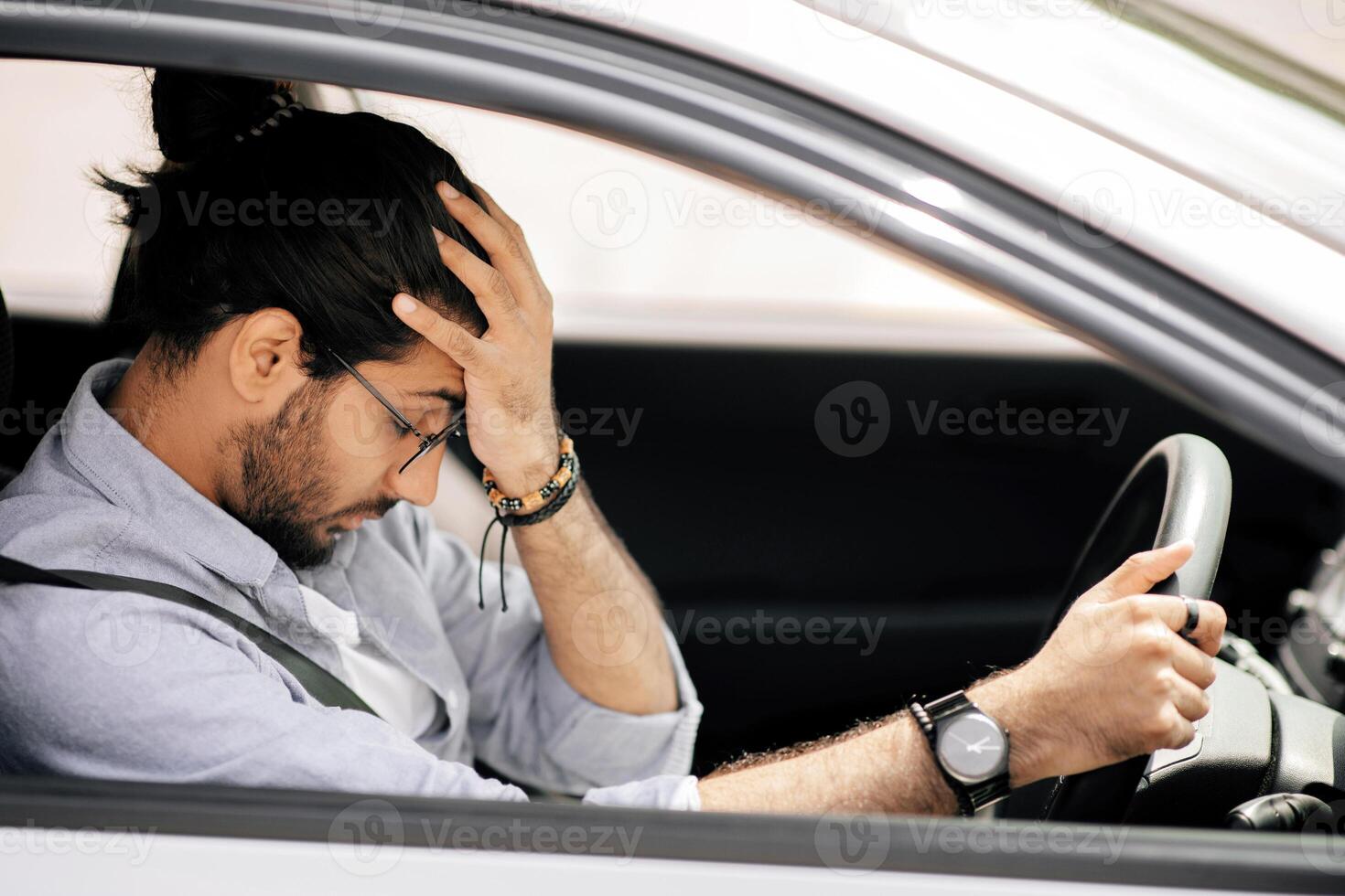 Stressful middle-eastern long-haired guy driving car, touching his head, getting late for business meeting or flight, stuck in traffic or got car crash, side view, closeup photo, copy space photo