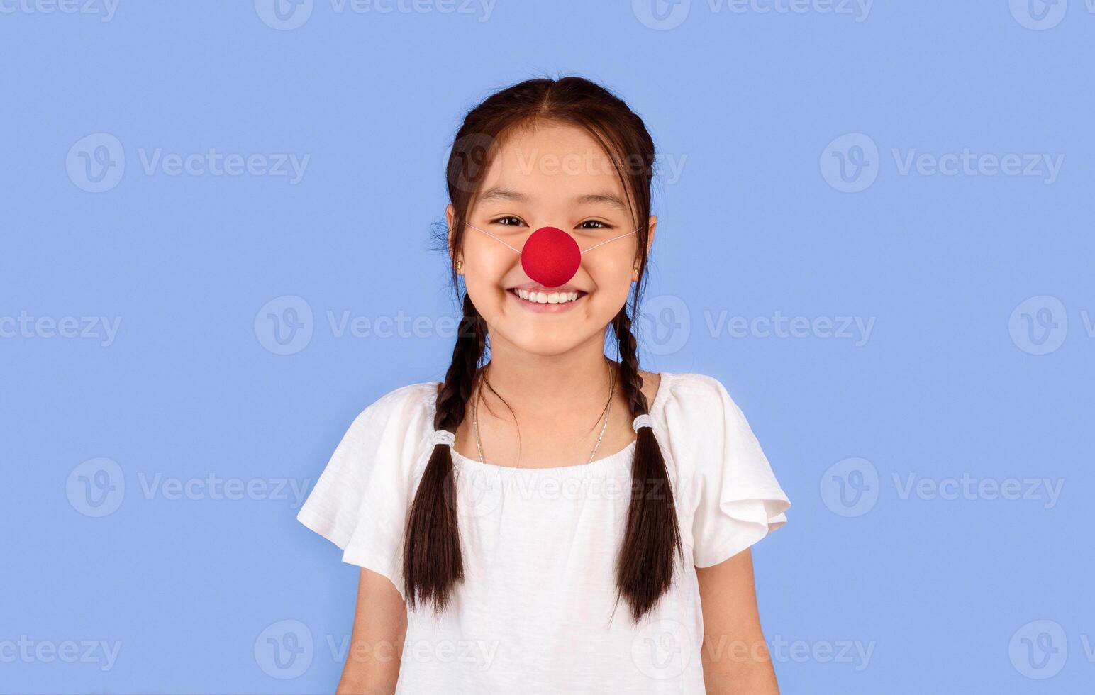 Funny Korean Kid Girl Wearing Clown's Nose Posing Smiling To Camera On Purple Background. Studio Shot photo