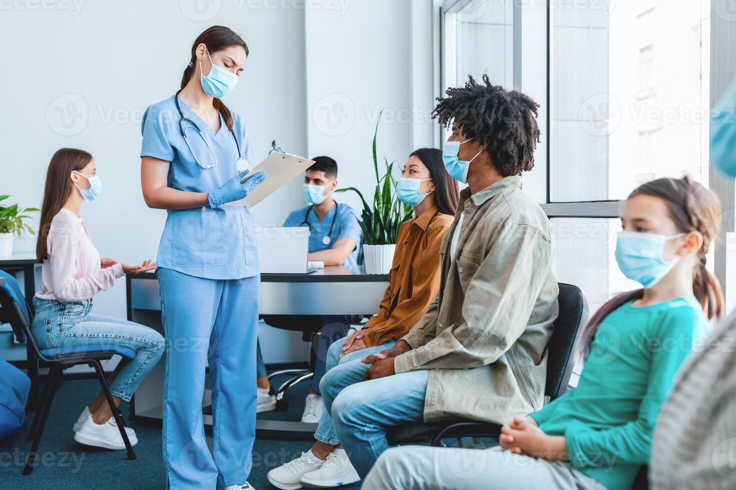 People in protective face mask waiting for vaccination against covid, sitting in queue line, multiethnic diverse group of patients getting ready for immunization at clinic, nurse writing photo