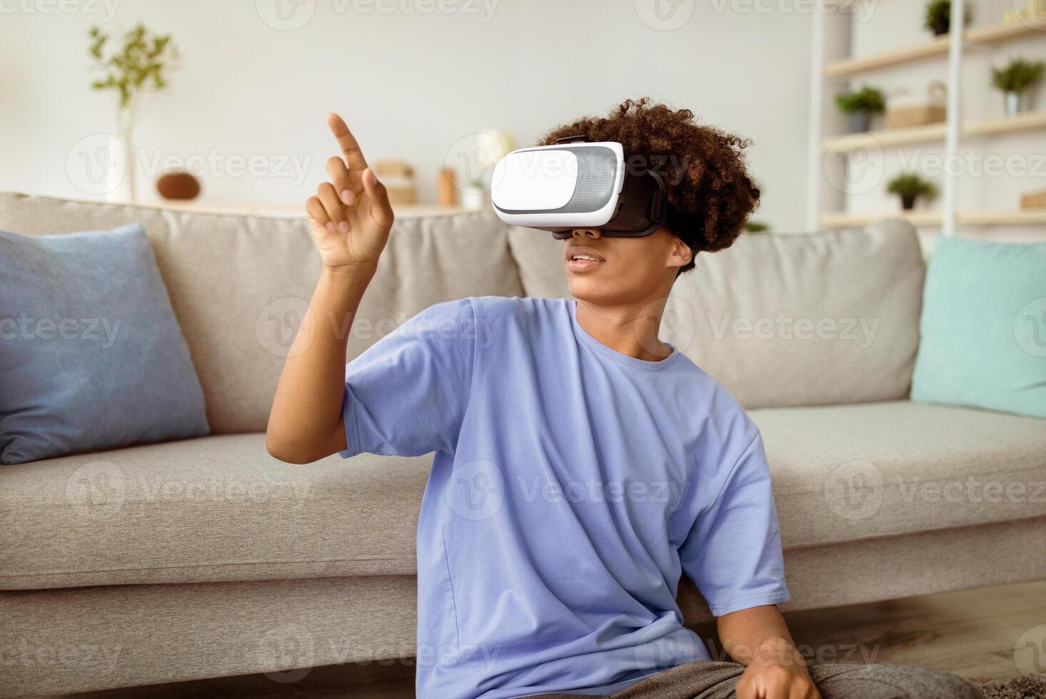 Modern technologies and entertainments. Cool black teen guy in VR headset exploring virtual reality at home, touching imaginary screen, interacting with cyberspace photo