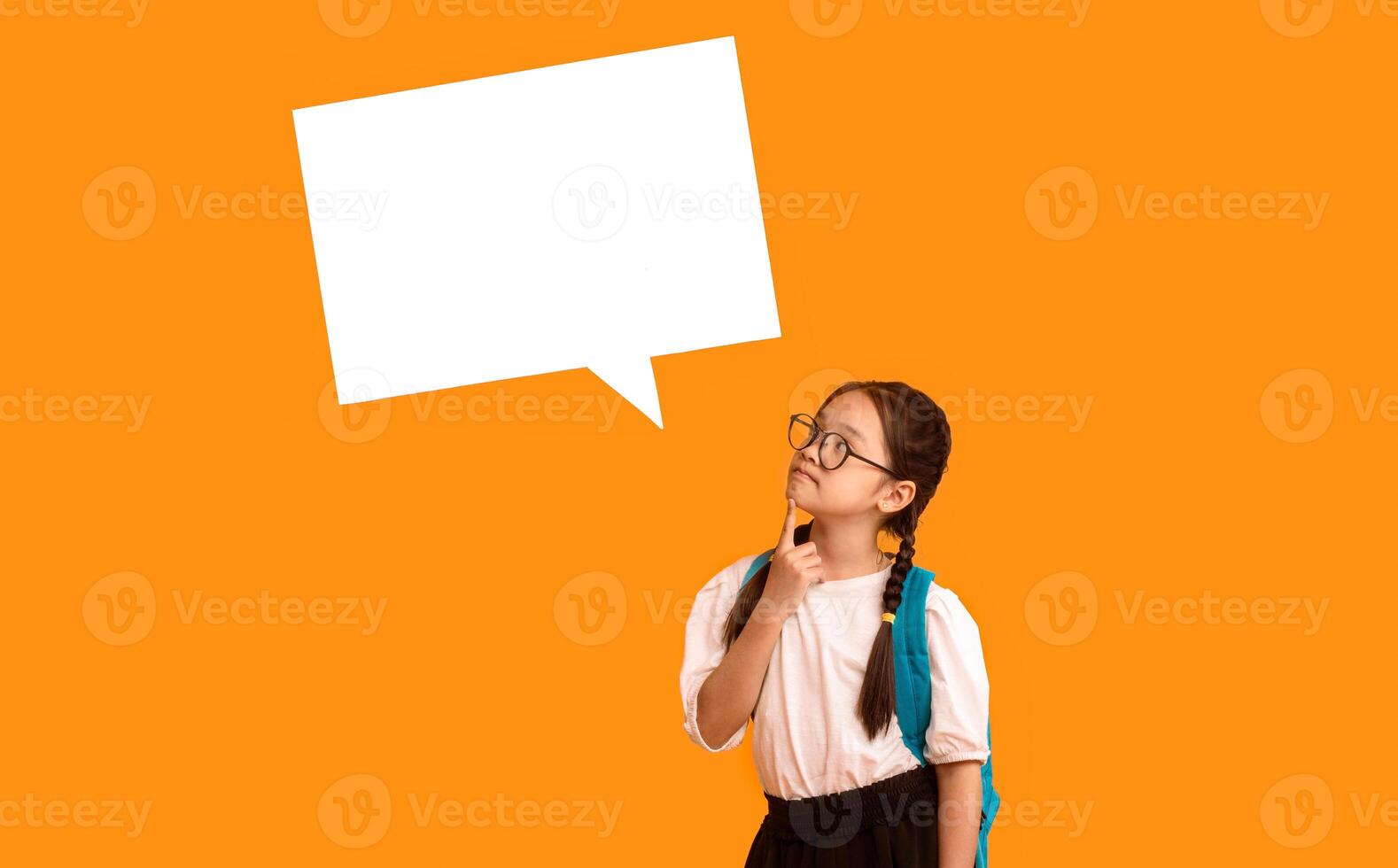 Asian Elementary School Girl Thinking Posing With Blank Speech Bubble Above Head On Yellow Studio Background. Mockup photo