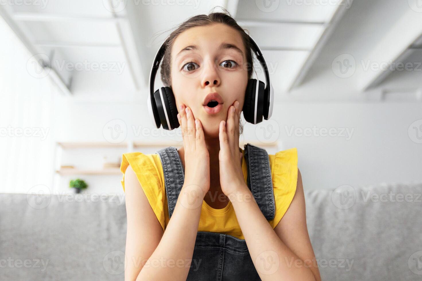 Omg, Unbeliveable. Portrait of surprised amazed schoolgirl in wireless headphones sitting at desk using laptop and looking at computer screen. Girl reading shocking breaking news, webcamera pov photo