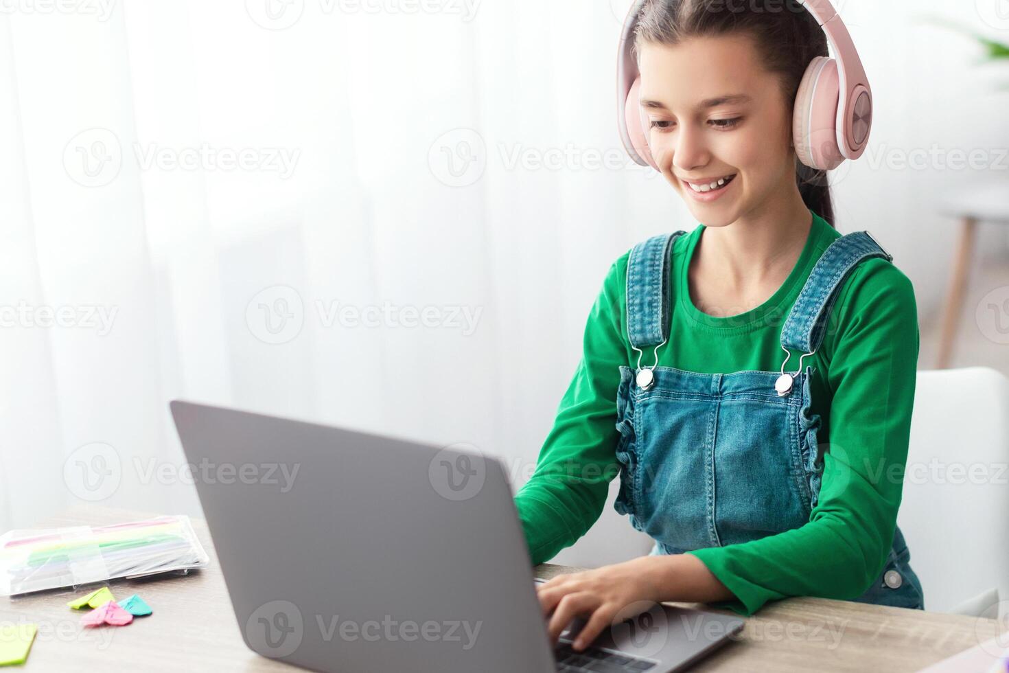 E-learning concept. Smiling female teenager studying online on laptop computer at home. Happy youth using PC to make home assignment, typing on keyboard, chatting with friends or doing homework photo