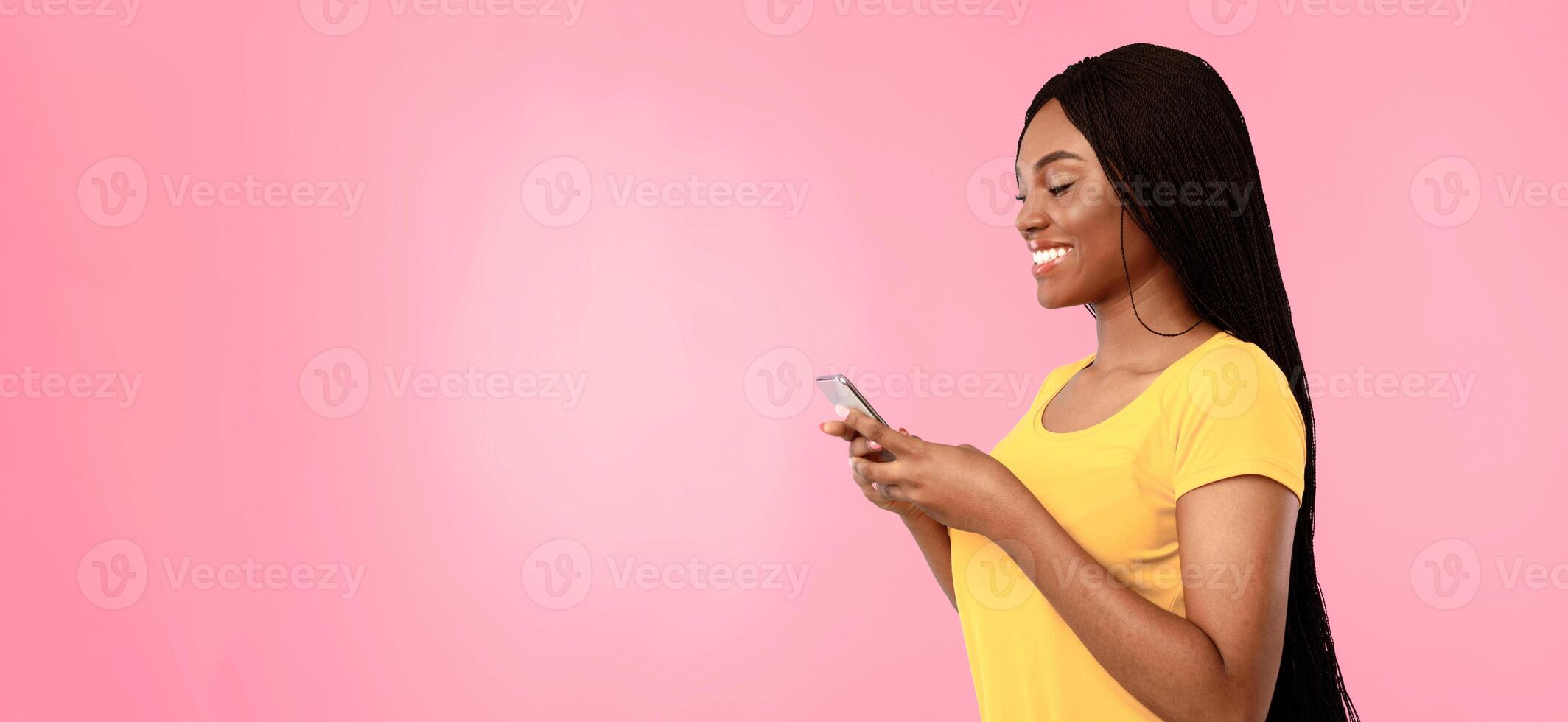 Side View Of Happy Black Woman Using Phone Texting And Browsing Internet Standing Over Blue Studio Background. New Application For Smartphone Concept, Blank Space For Advertisement Text photo