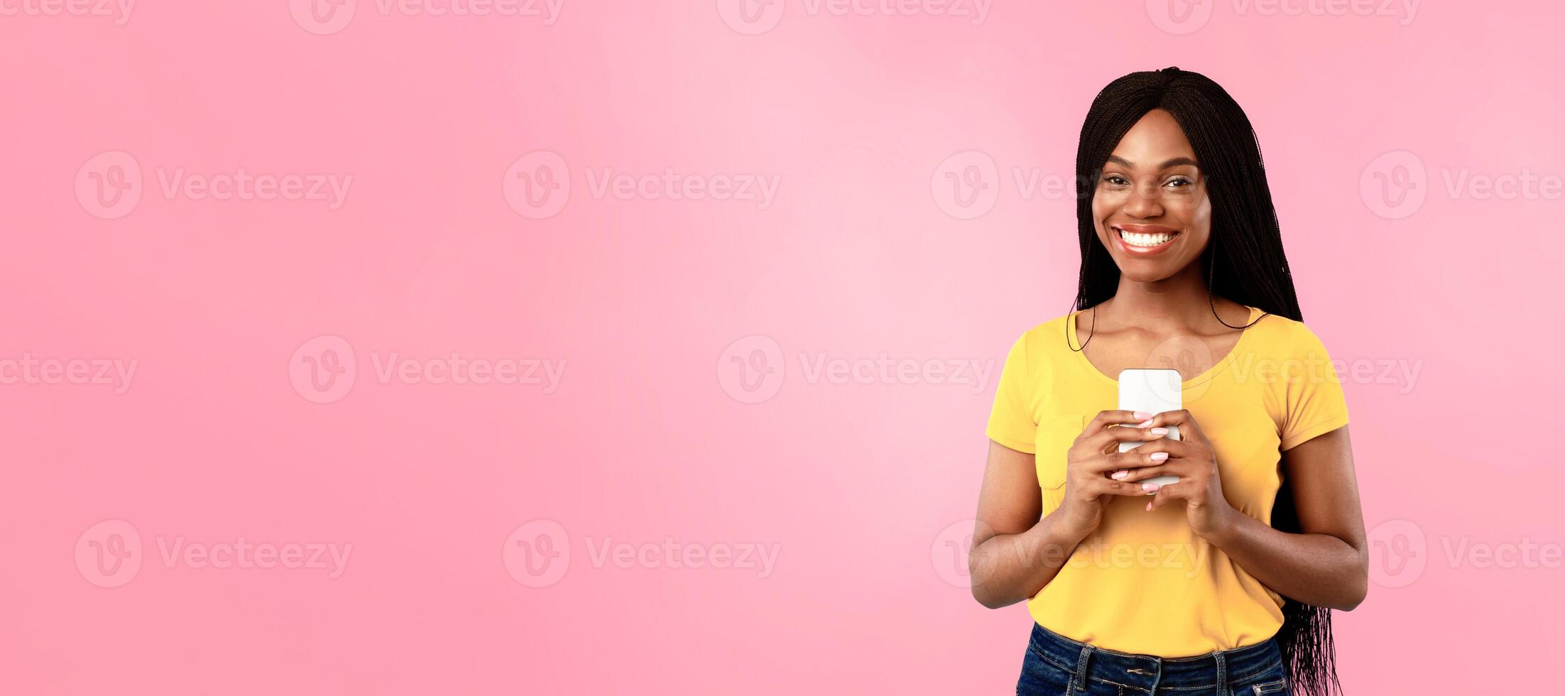 African American Female Holding Smartphone Posing Over Blue Background In Studio, Smiling To Camera. Black Millennial Woman Using New Application On Mobile Phone Texting And Browsing Internet photo