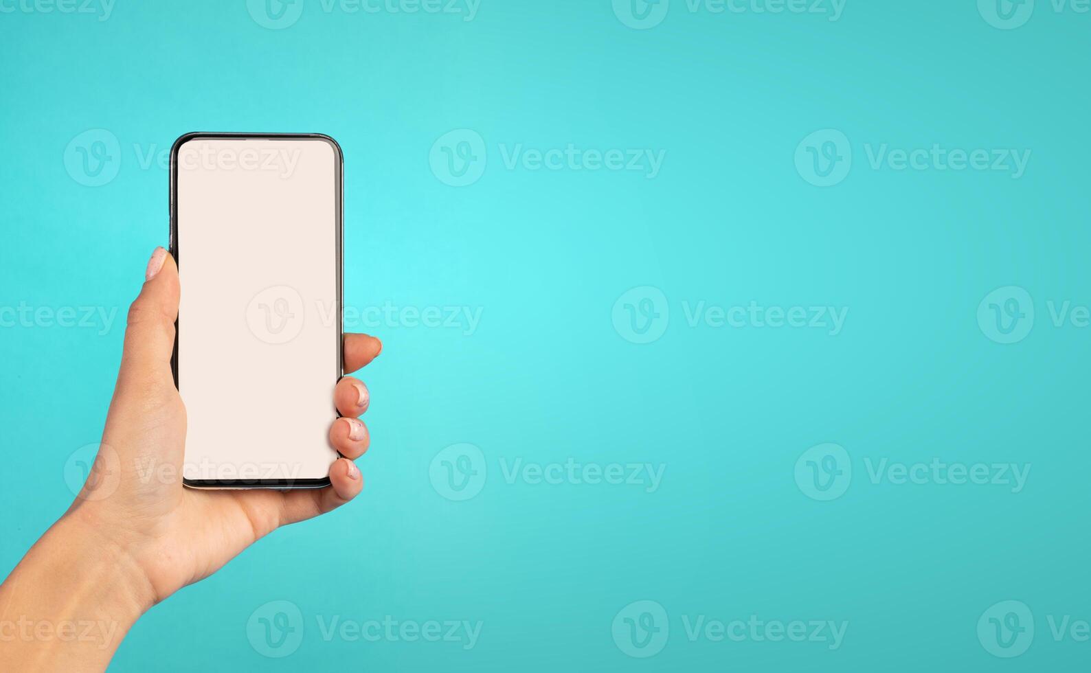 Female Hand Holding Mobile Phone With Blank White Screen Showing Smartphone Empty Display Advertising Application For Cellphone Over Blue Studio Background. Woman Recommending App. Mockup, Closeup photo