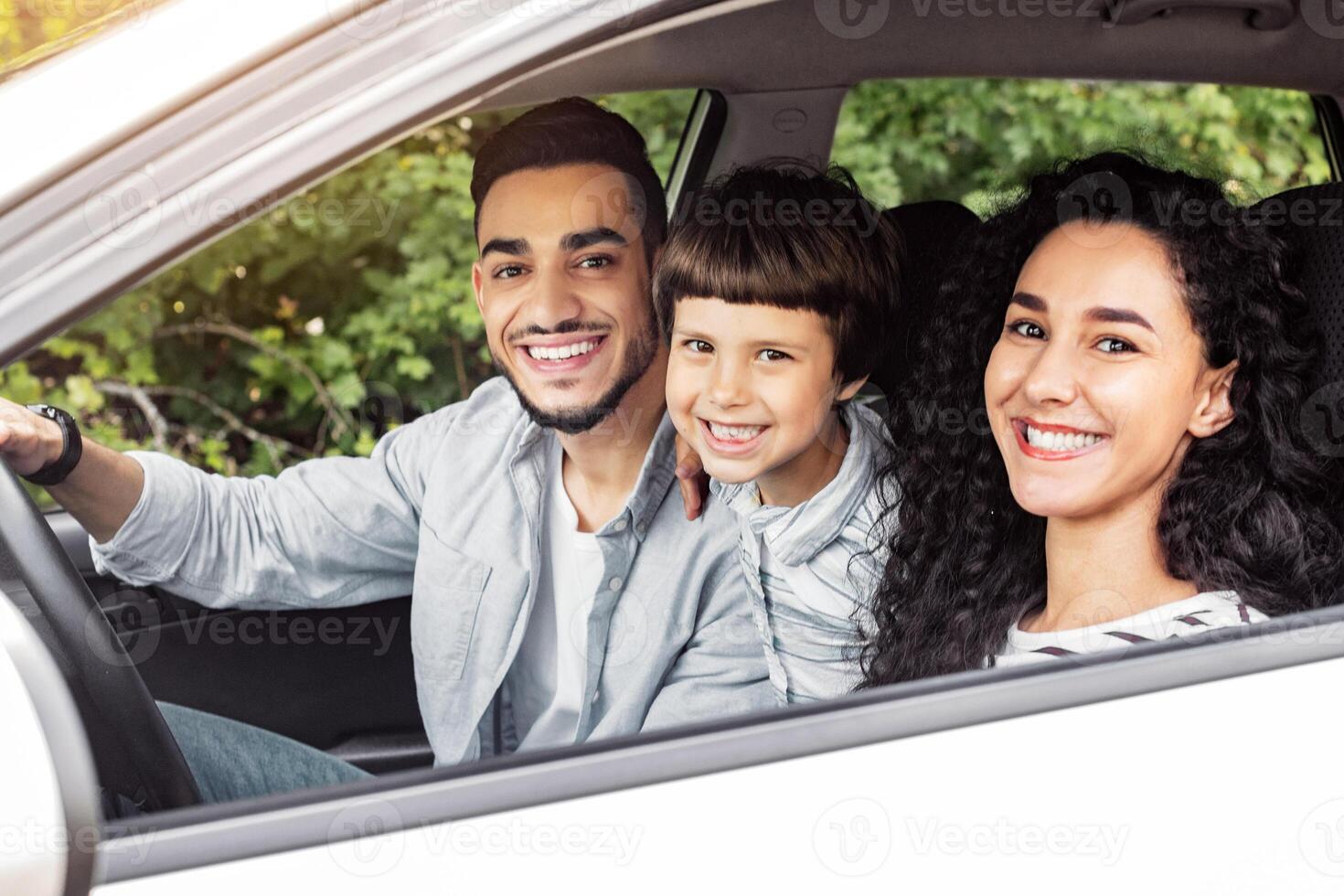Happy millennial middle eastern family with child go to vacation by car and look at camera, copy space. Family trip on new auto, weekend together, love and relationship, journey and facial expression photo