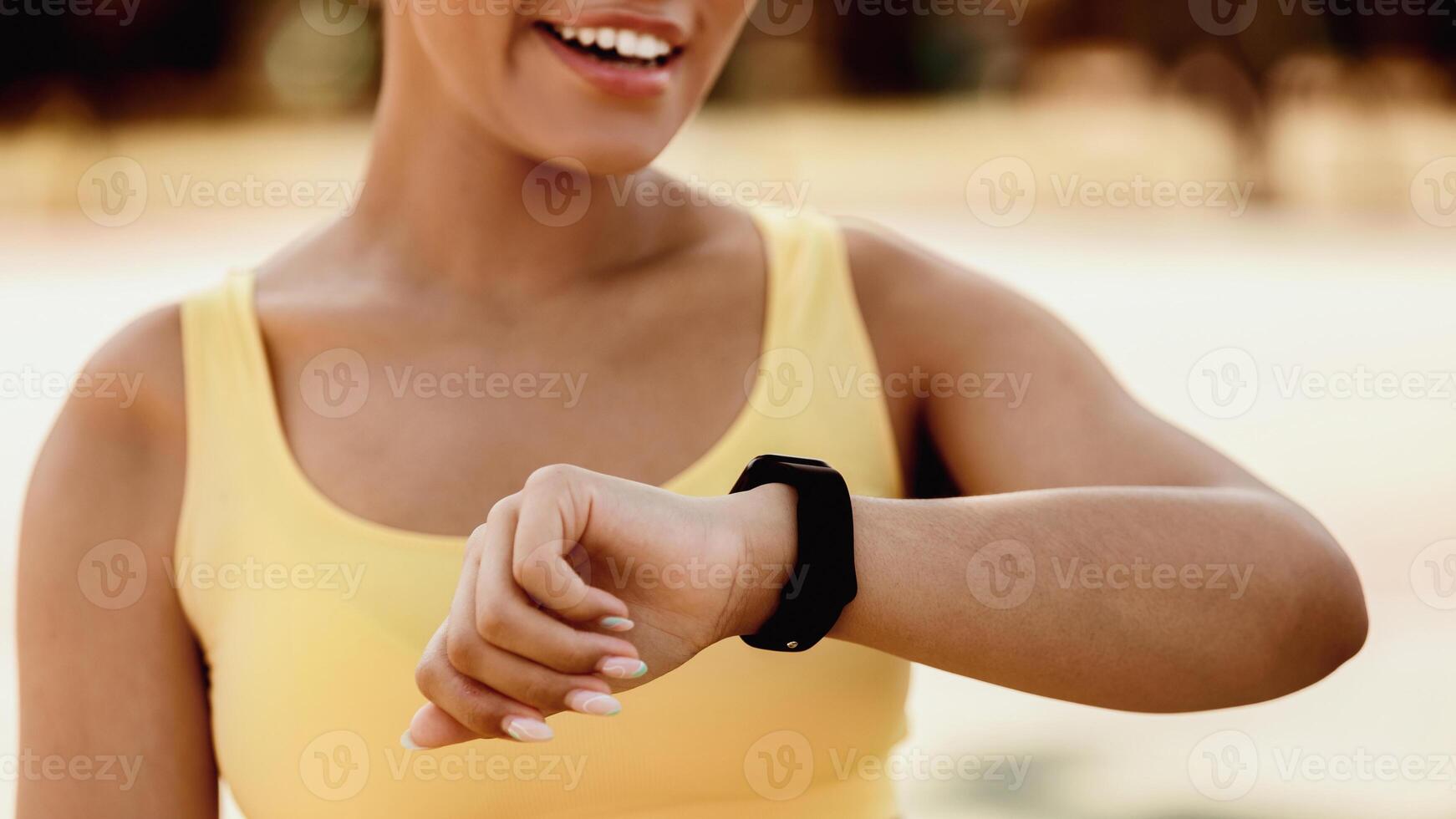 Closeup cropped view of smiling African American lady using smartwatch to monitor progress. Female athlete checking her performance and running trail looking on wearable fitness wristwatch device photo
