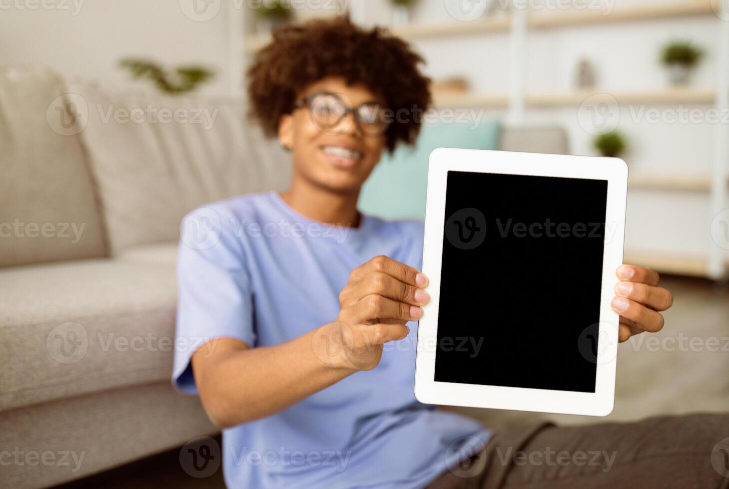 Positive black teenager showing tablet pc with blank screen at home, mockup for mobile app or website design. Online studies, remote communication during coronavirus quarantine photo