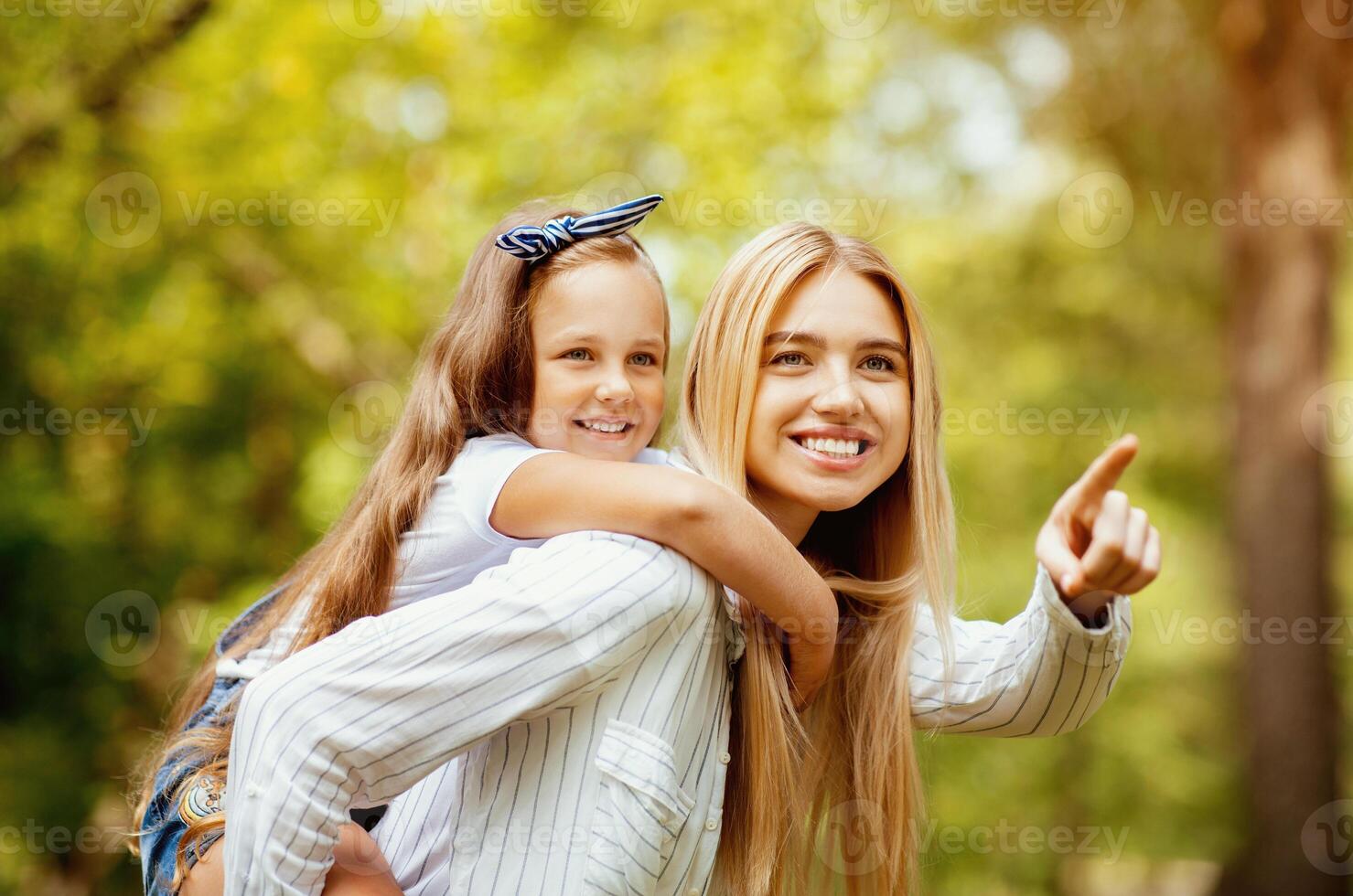 Look There. Mother Carrying Daughter Piggyback And Pointing Finger Spending Time Walking Together In Park Outdoor On Weekend photo
