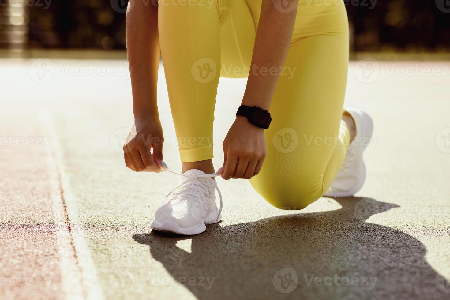 Training Concept. Closeup cropped view of unrecognizable black female athlete in bright yellow leggings tying her shoelaces before jogging outdoors in the morning, wearing white sneakers photo