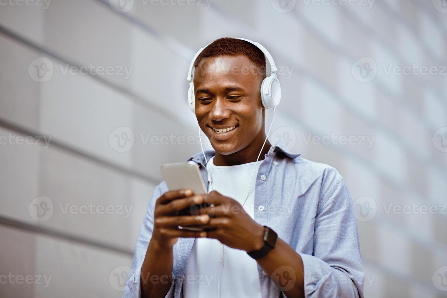 Cheerful African American man in headphones picking music playlist on smartphone near brick wall outside photo