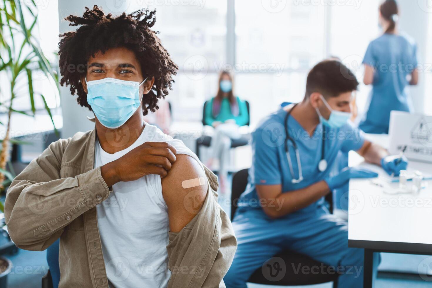 flu Vaccination Concept. Happy African American Guy In Surgical Mask Showing Vaccinated Arm With Adhesive Bandage Plaster On Shoulder After Getting Corona Virus Vaccine. Antiviral Injection photo