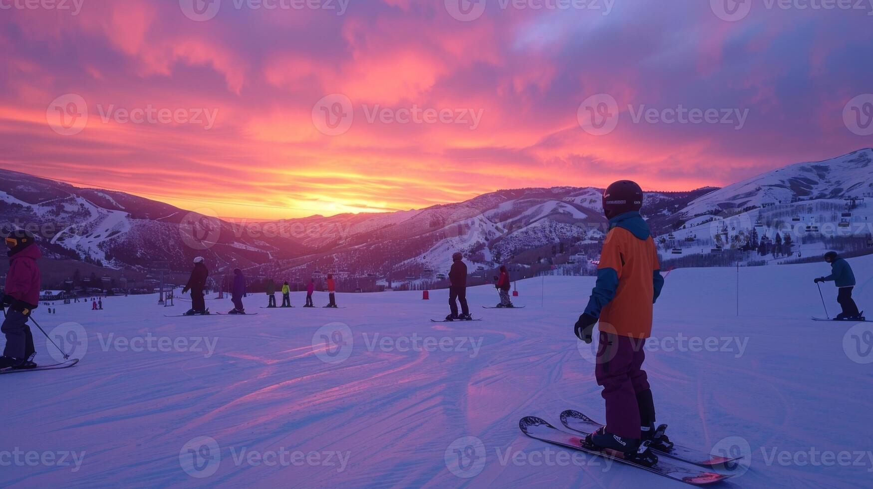A group of skiers gathers on a ski slope as the sky fills with vibrant colors during sunset, creating a picturesque winter atmosphere in the mountains. photo