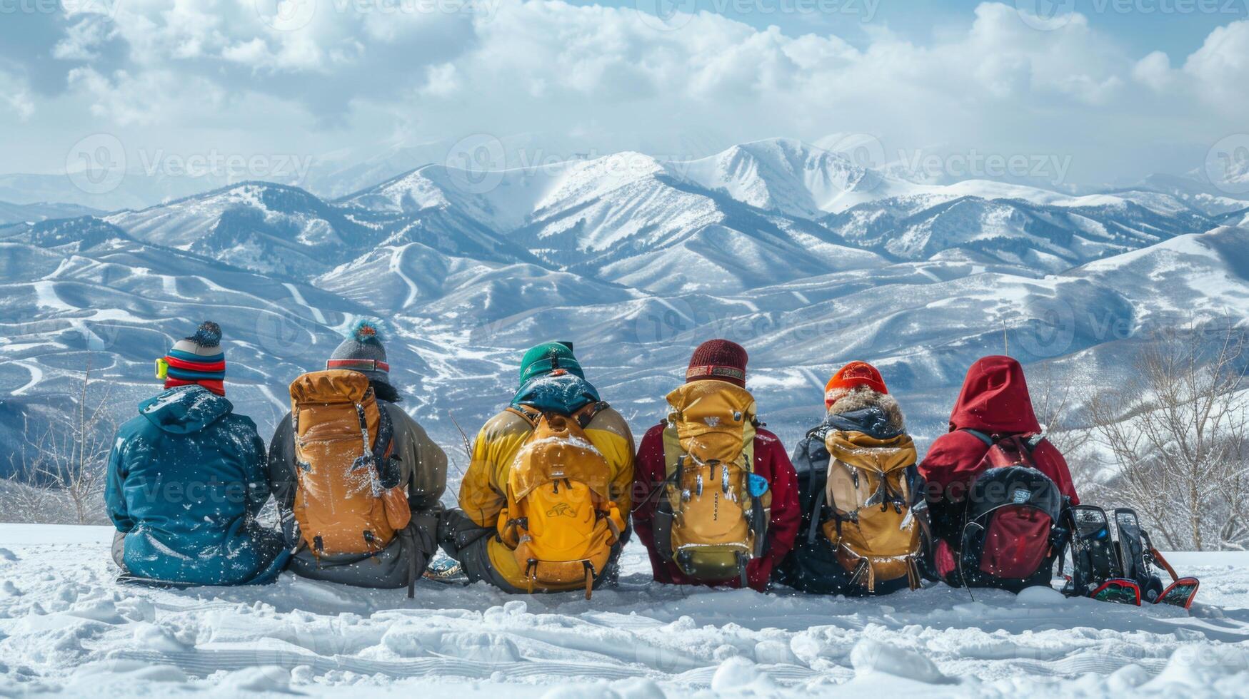A group of six hikers sits side by side on a snowy mountain slope, gazing out at majestic peaks under a clear blue sky. The bright sun casts shadows across the landscape. photo