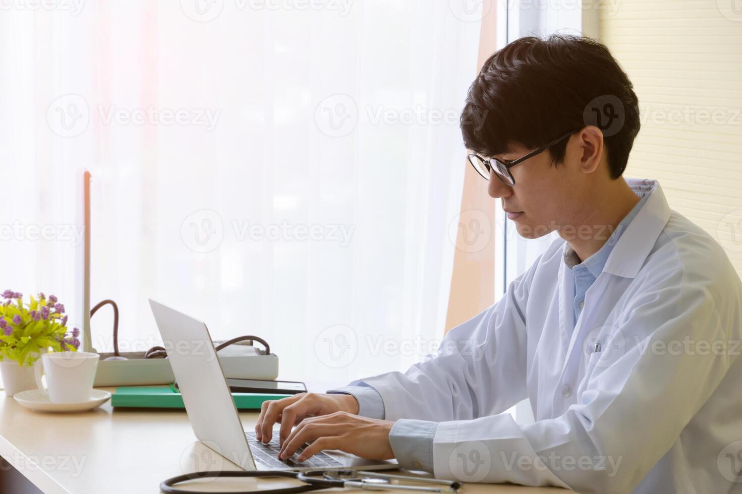 Male doctor sitting at desk and working with laptop in hospital office photo