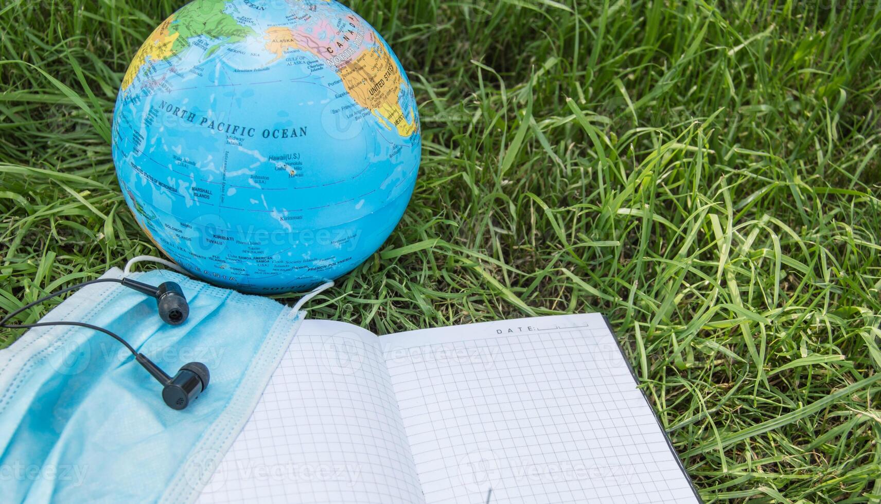 A globe, a mask and a notebook on the grass photo