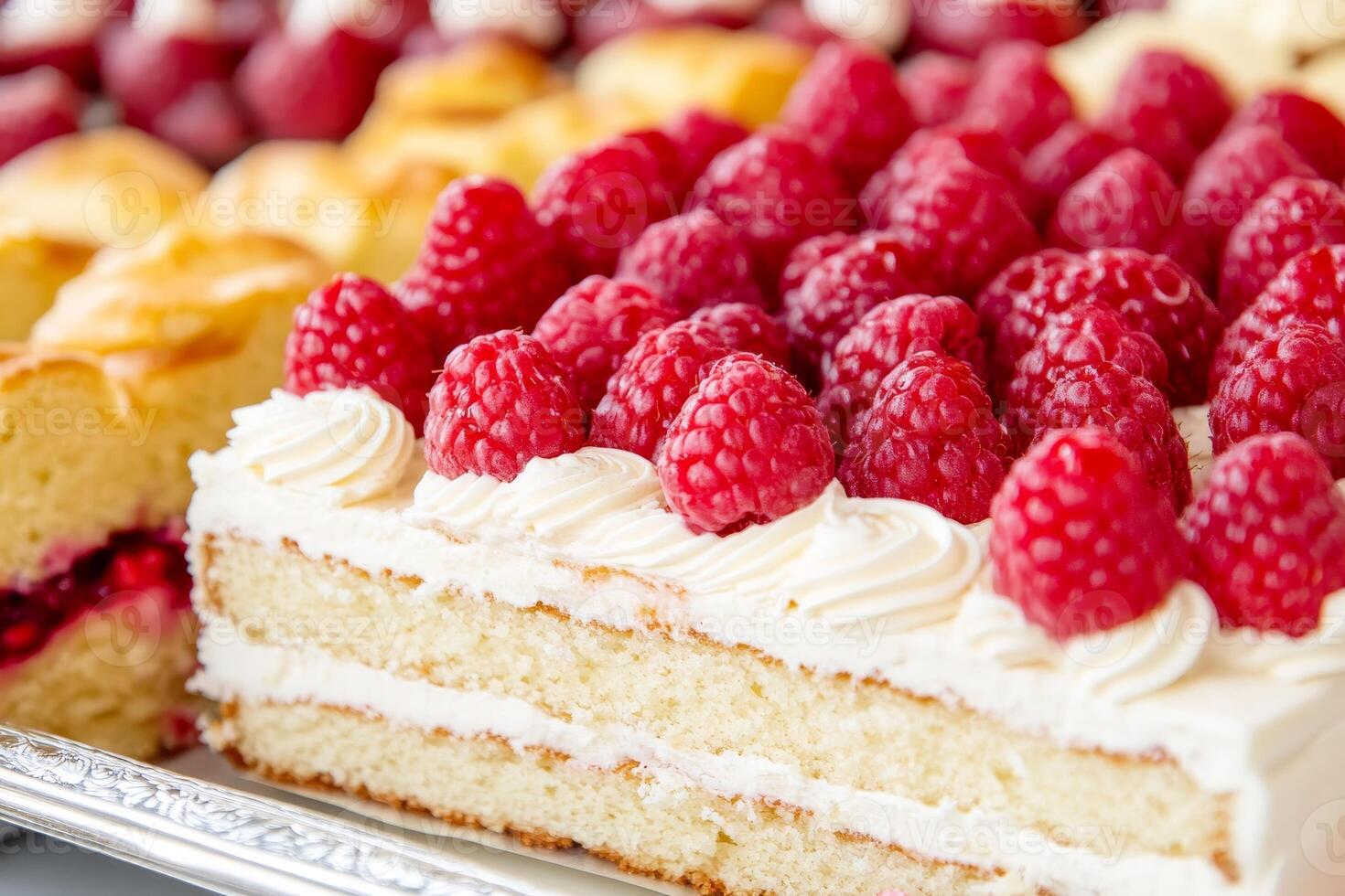 A lavish tray features an array of decadent desserts, prominently displaying a raspberry cake adorned with plump, fresh raspberries. Sweet treats await indulgence photo
