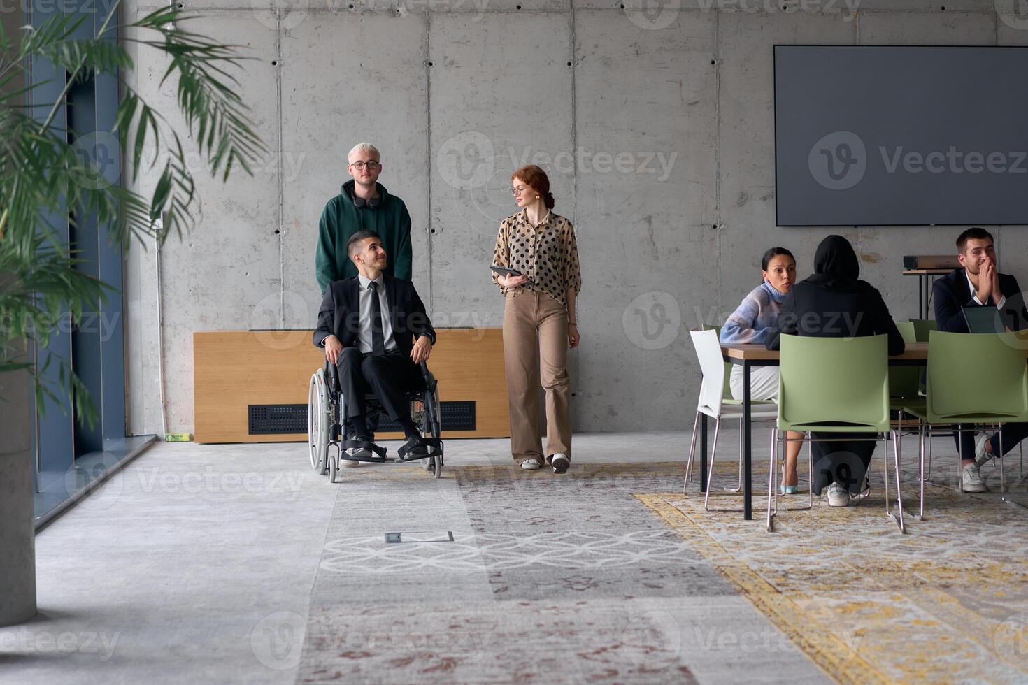 A diverse team of business colleagues, including a director in a wheelchair, engages in a collaborative discussion as they move together through a modern office space photo