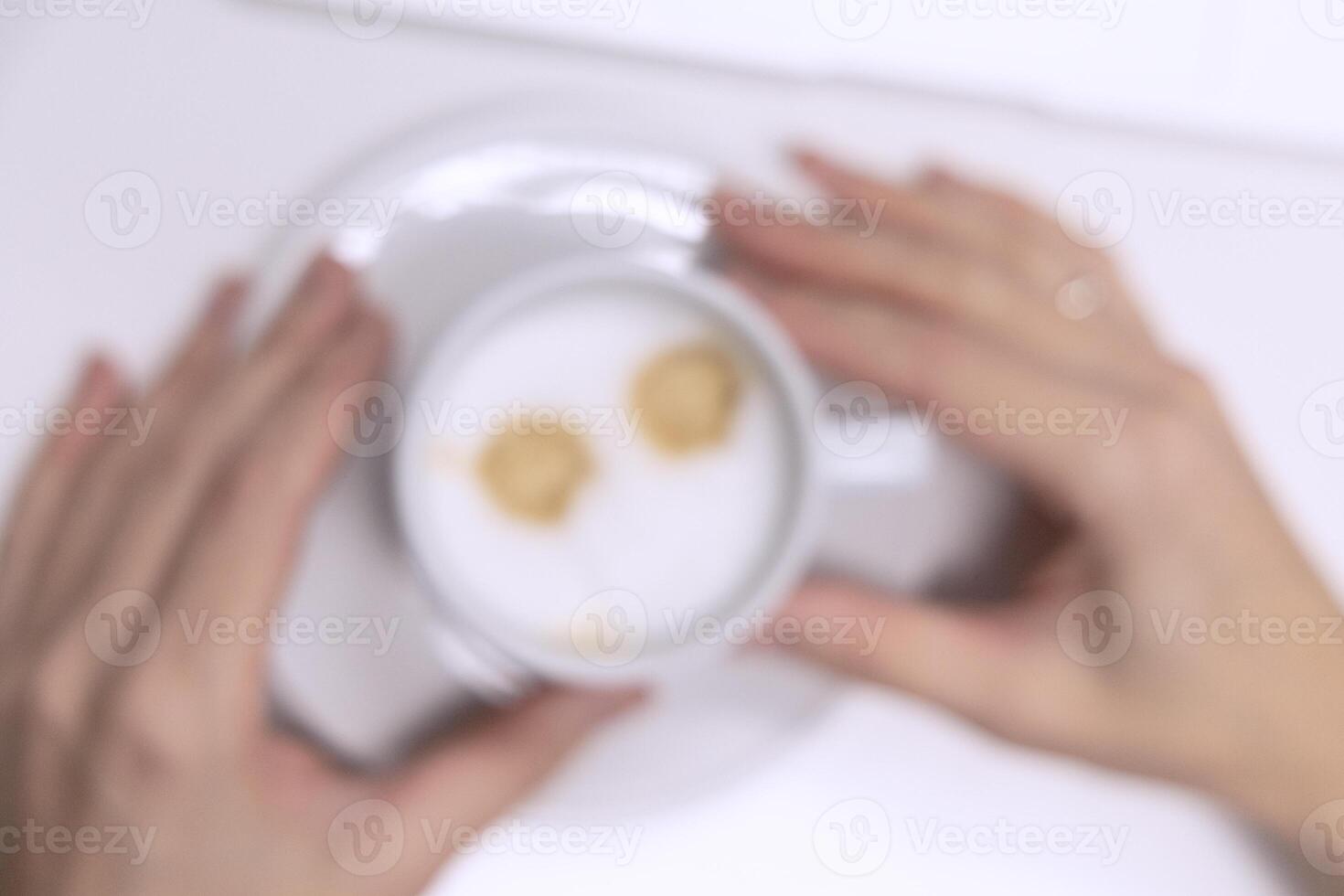 Cup of coffee on the table in the office in female hands, view from above. Blurred background photo