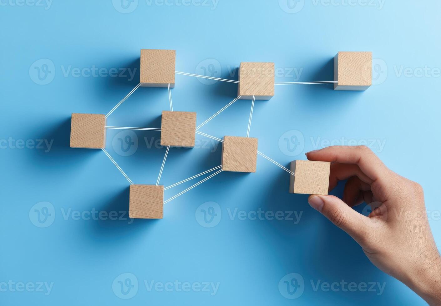 A hand connecting wooden blocks on a blue background, symbolizing networking, strategy, and teamwork in business. photo