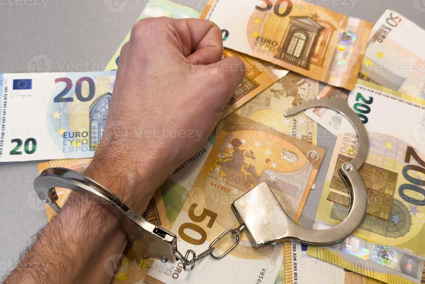 Folded hands and handcuffed hands resting on a table in front of money. photo