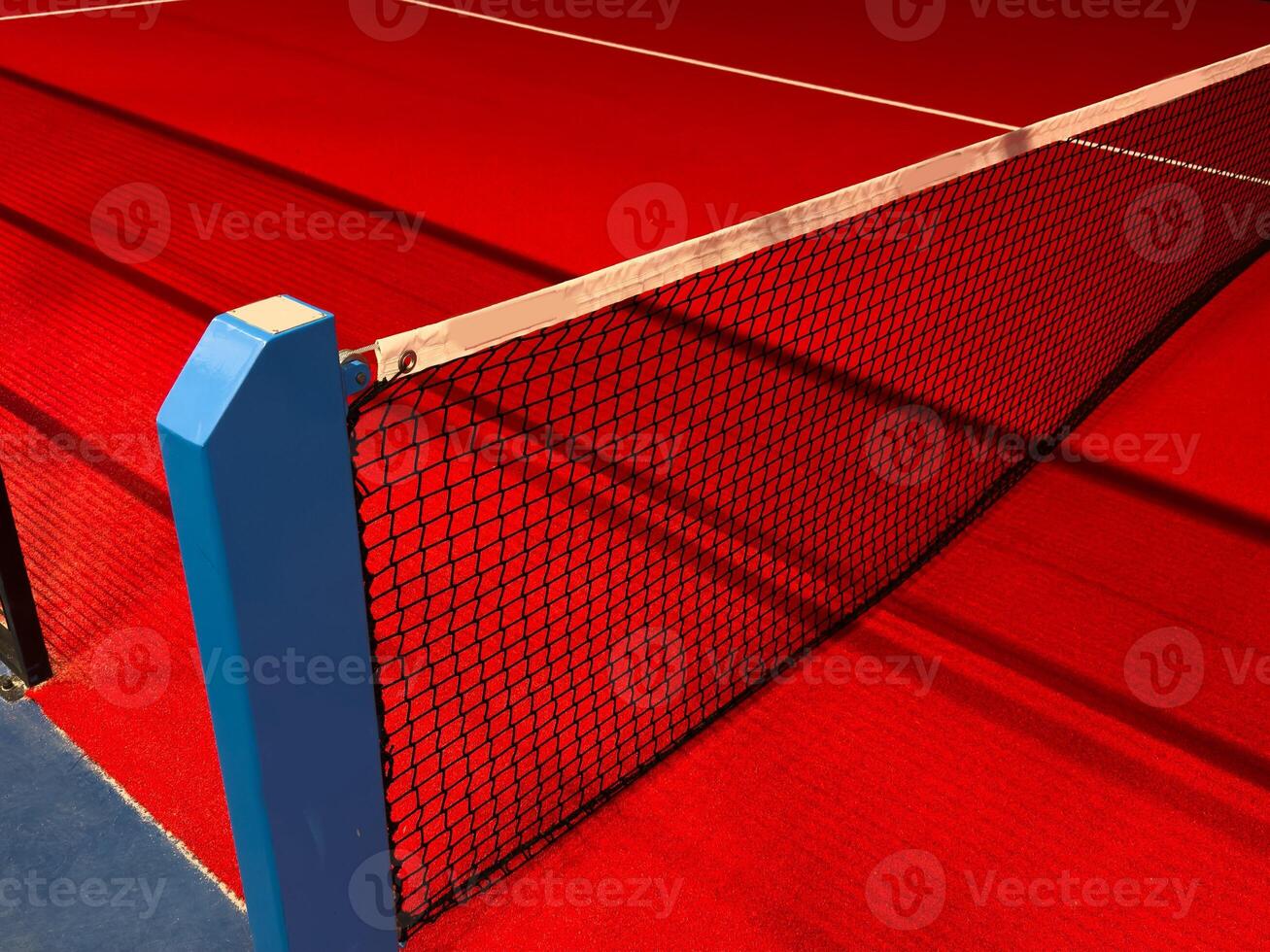 View of the net and the centre line of a red paddle tennis court. Racket sports photo