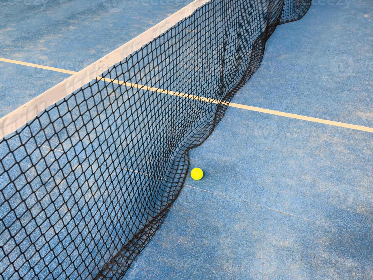 Ball in the shade of the net of a blue paddle tennis court. photo