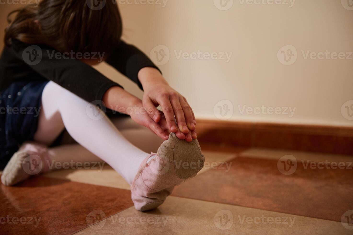 Young dancer stretching on the floor wearing ballet slippers and tights indoors photo