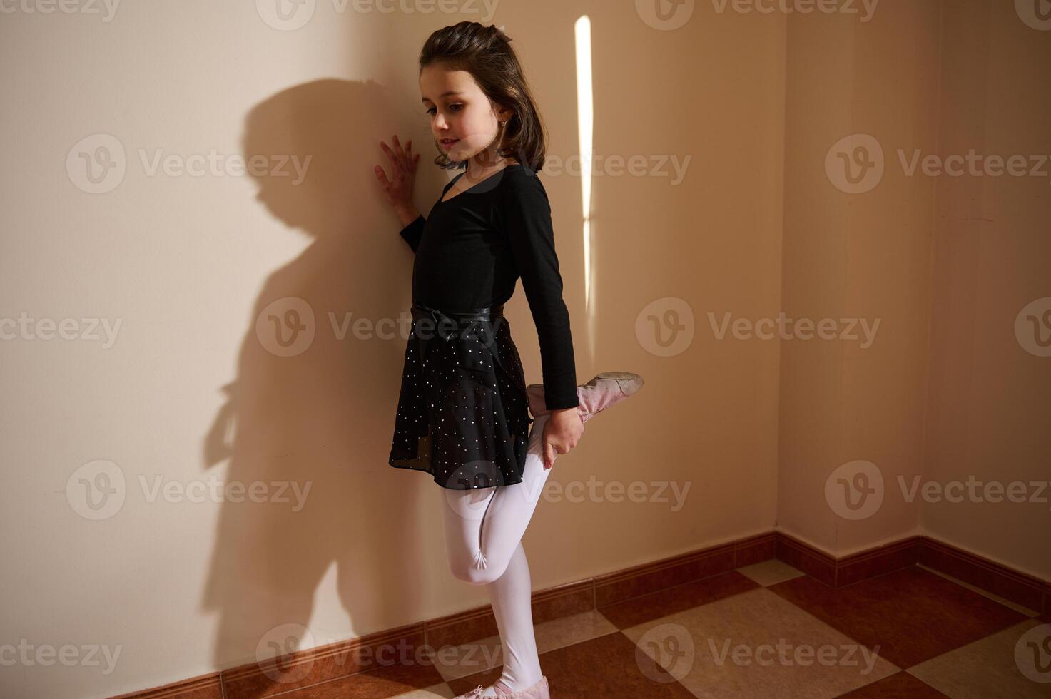Young dancer stretching leg against wall at home in natural light photo