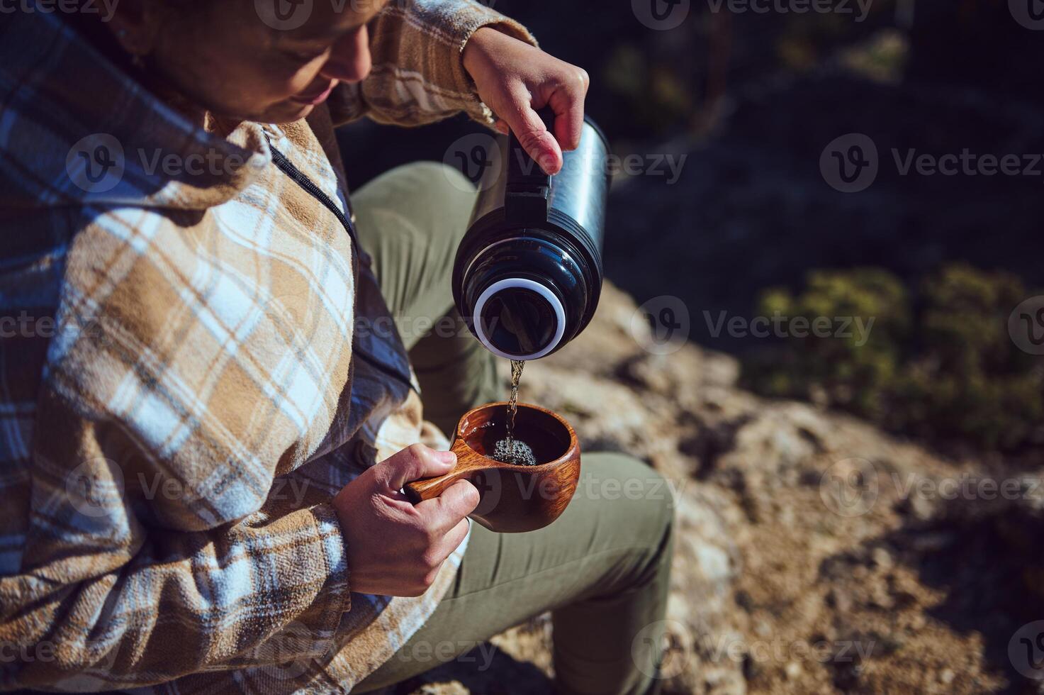 Person enjoying outdoor coffee in nature by pouring beverage from thermos photo