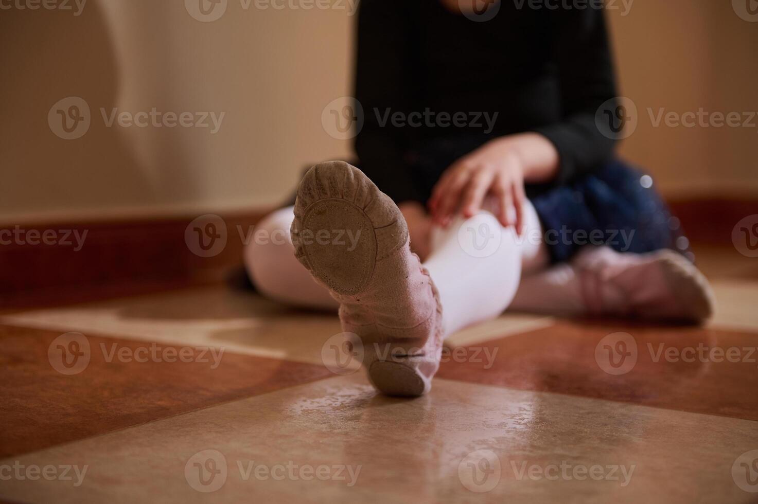 Close-up of a young child sitting on a tiled floor wearing tights and ballet shoes. photo