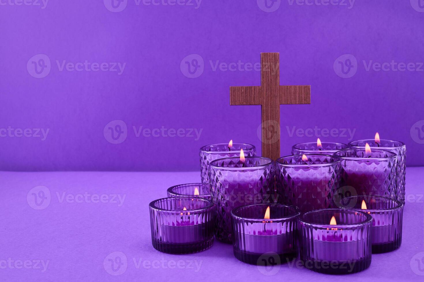 Lent Symbolism. Cluster of lit candles with a cross on a purple background. photo