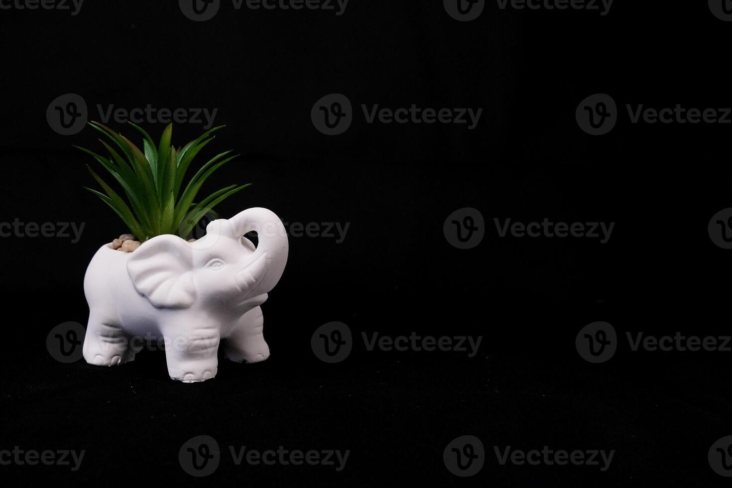 White ceramic elephant with green grass on black solid background photo