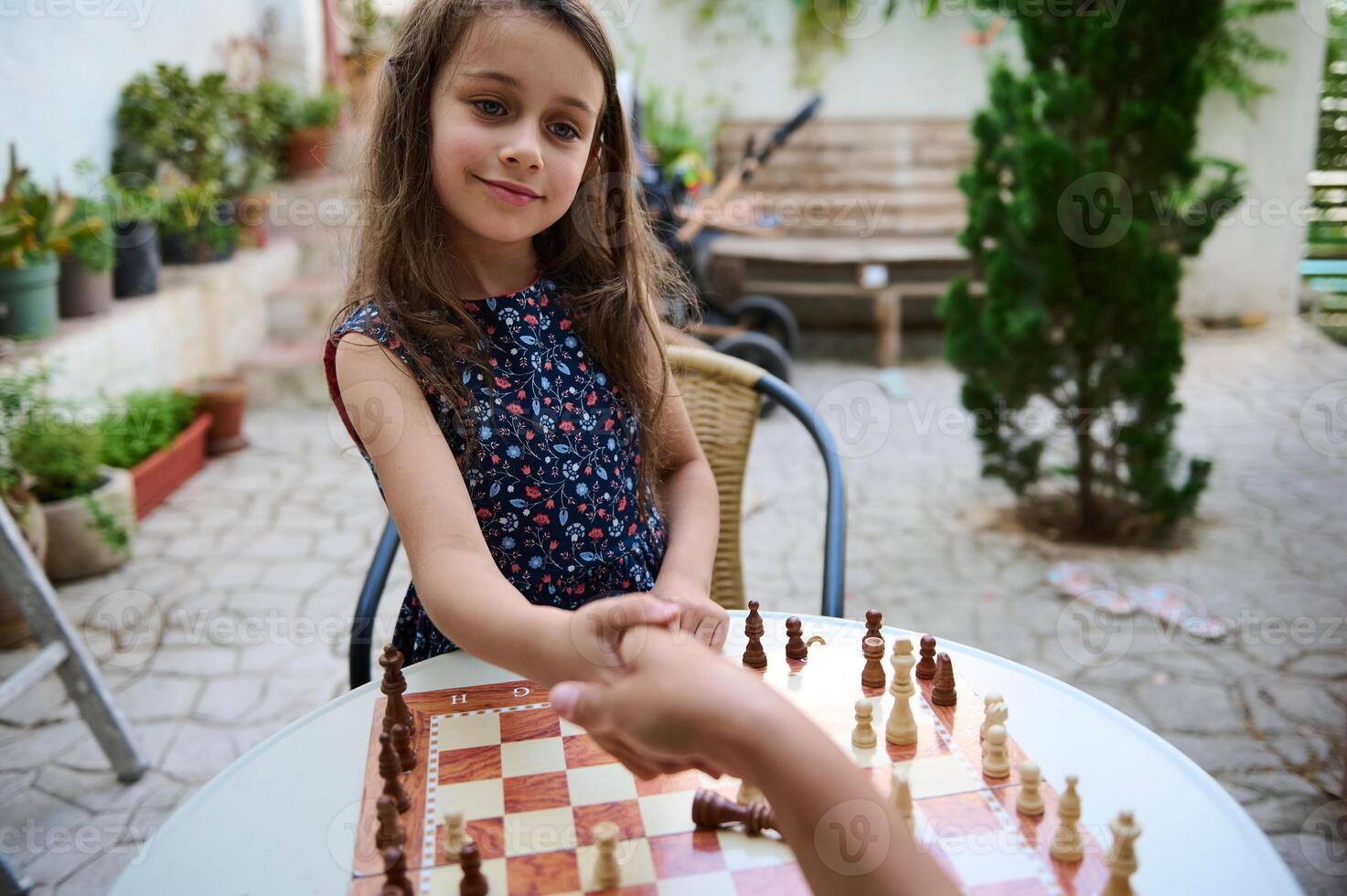 Smiling Girl Shaking Hands After a Chess Match in a Courtyard photo