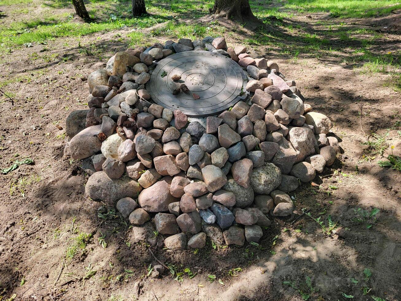 The cast-iron hatch is decorated with cobblestones, fallen fir cones are on the hatch cover. photo