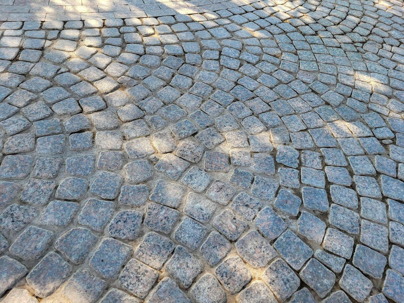 The sidewalk is made of gray square paving stones with shade from the foliage of trees photo