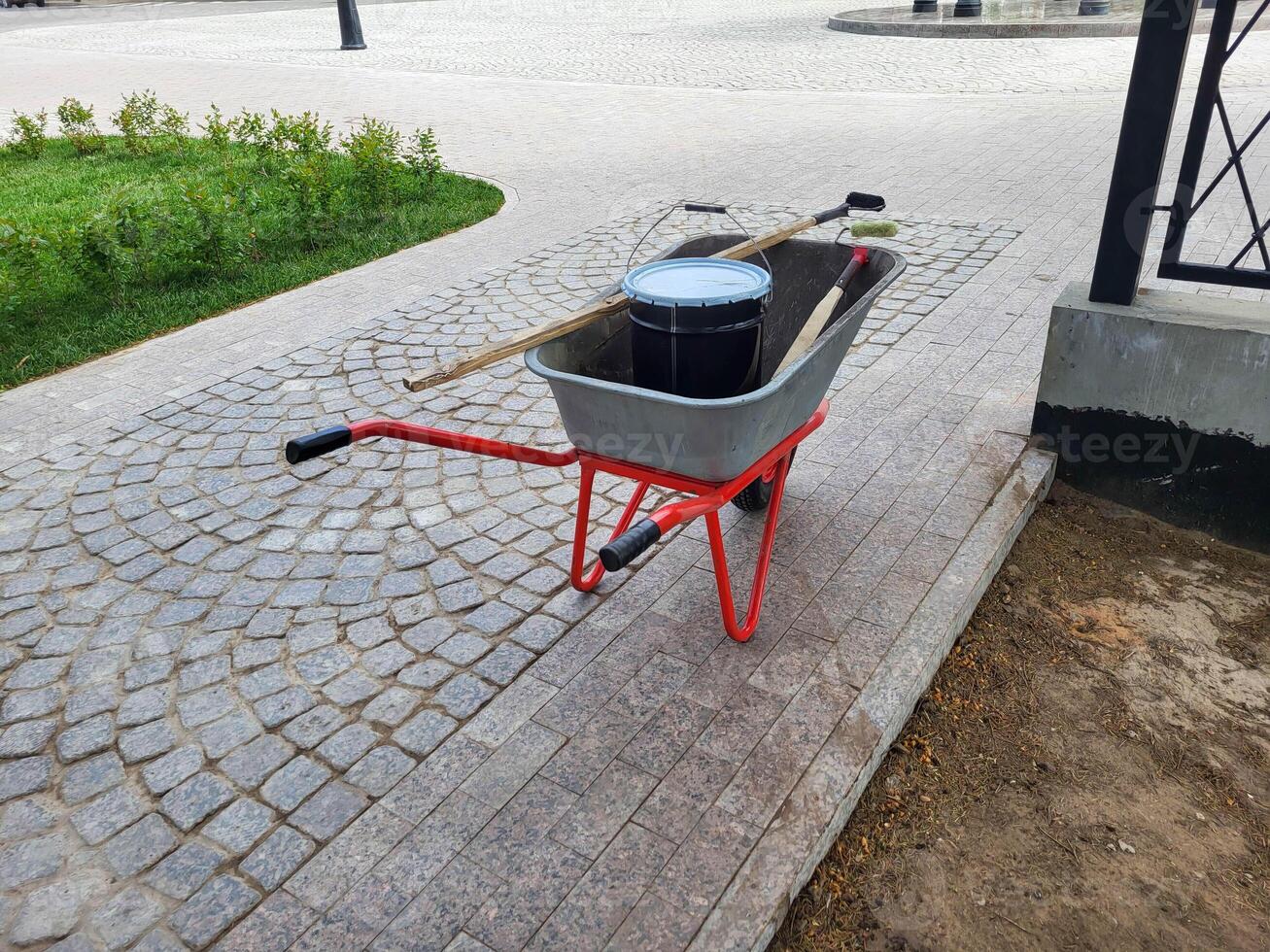 An iron wheelbarrow with red handles for transporting building materials in the garden and backyard. photo