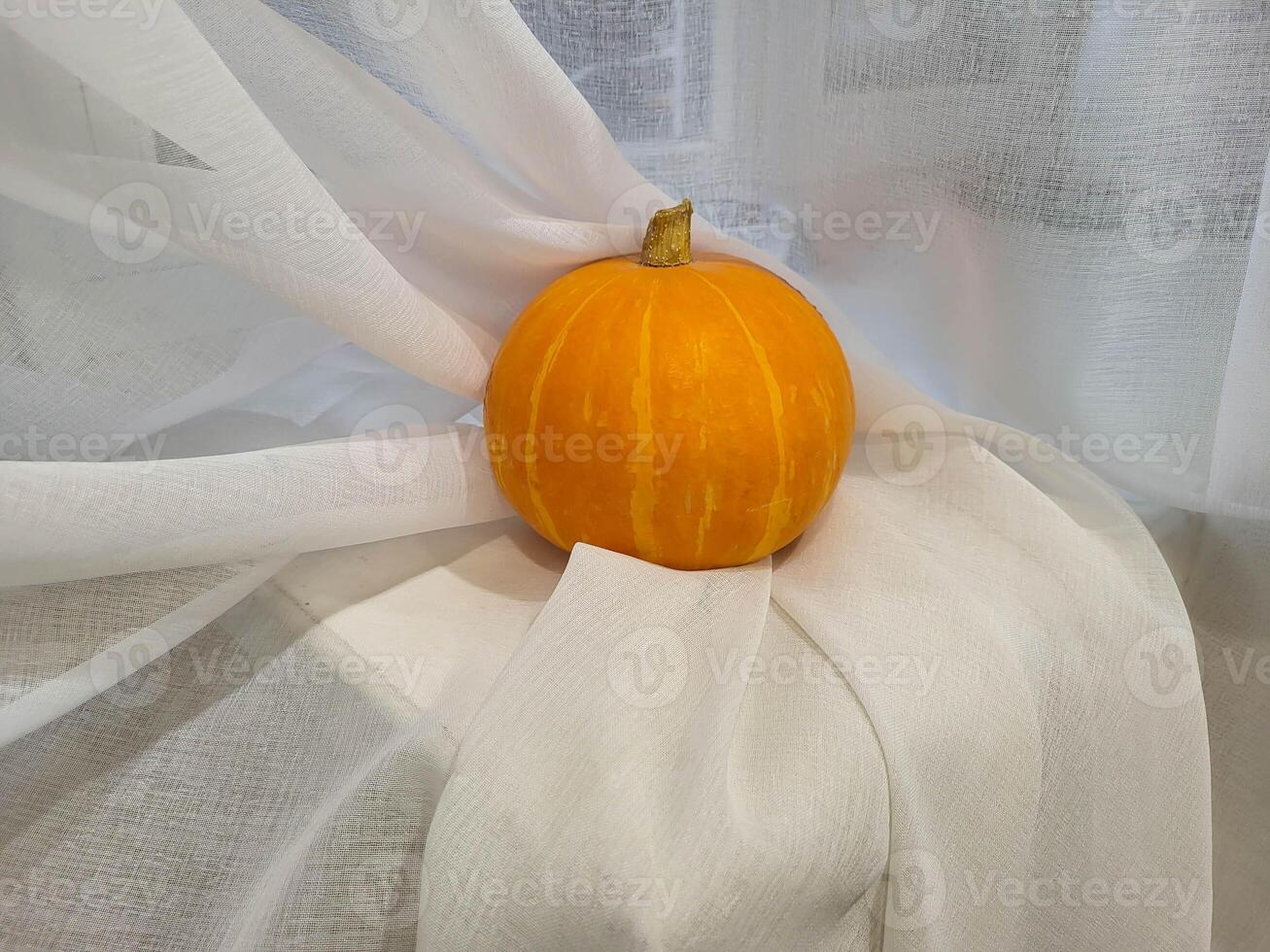 An orange pumpkin, lying on a white cloth background photo
